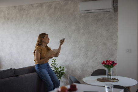 woman fanning herself while adjusting the AC temperature