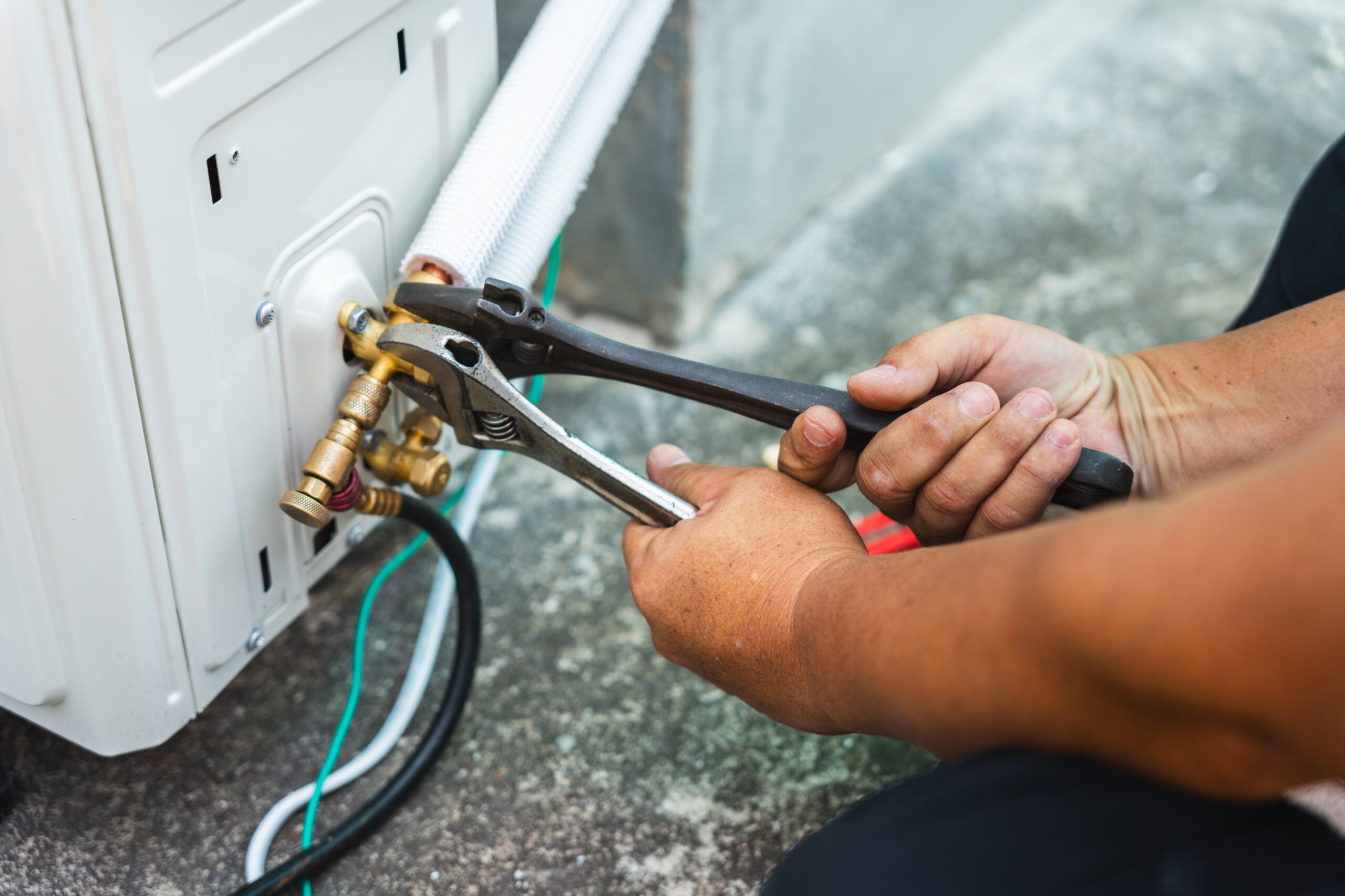 Air conditioner technician hands using wrenches to tighten flare nut on outdoor unit during installation, HVAC contractor repairing a split system air conditioning compressor with hand tools
