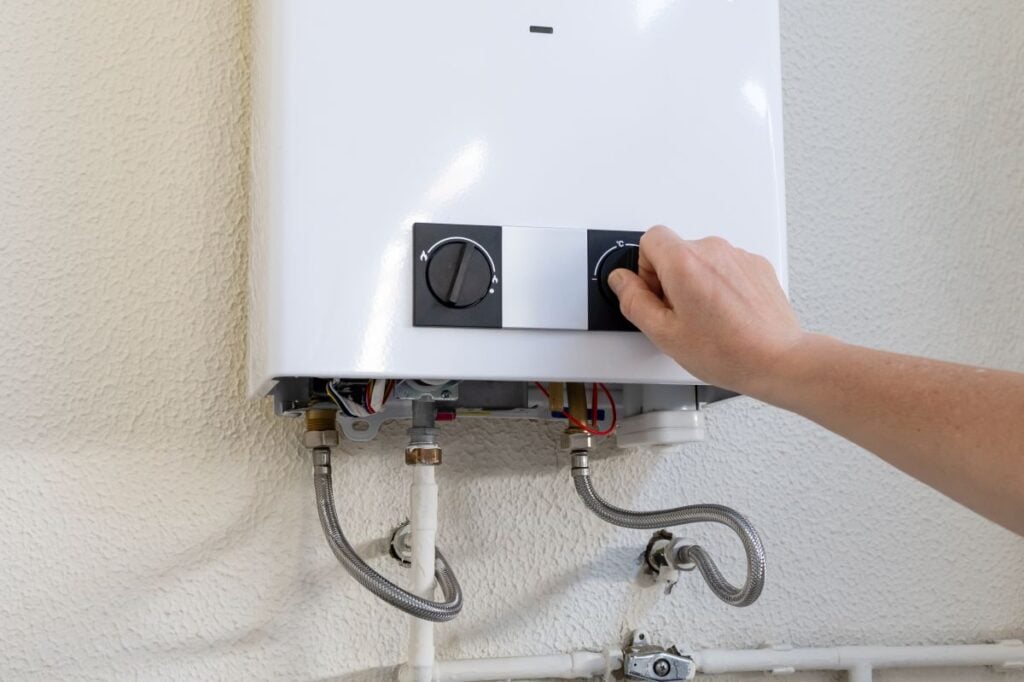 Person's hand turning a knob on a white wall-mounted gas water heater