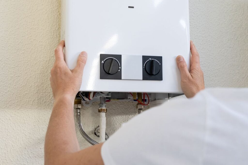 Professional plumber mounting a modern tankless gas water heater on an interior wall