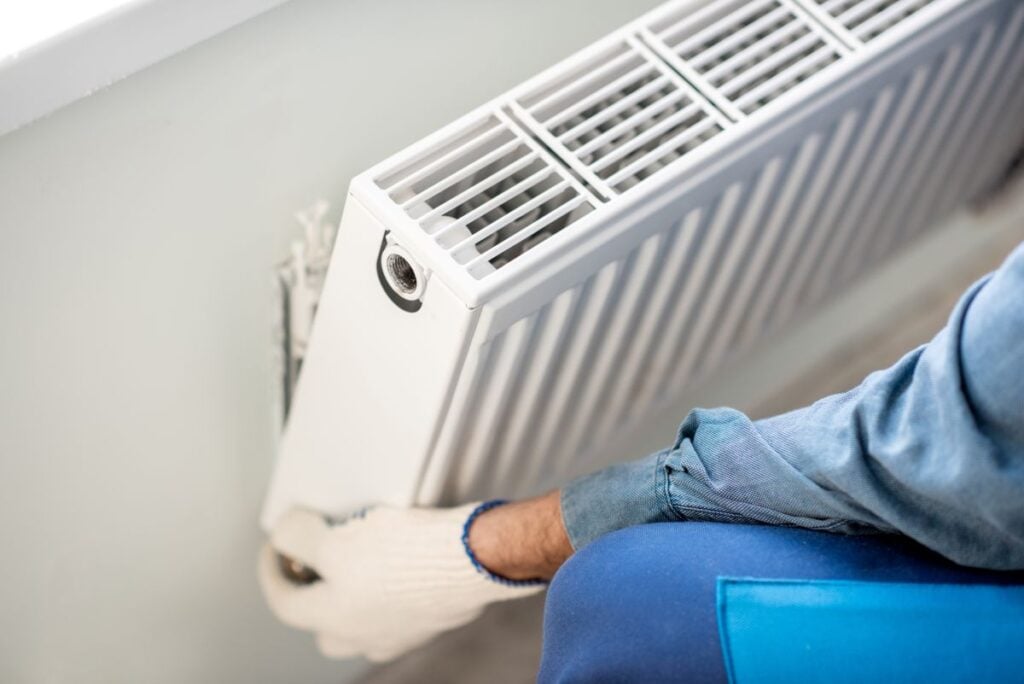 Workman mounting water heating radiator on the white wall indoors