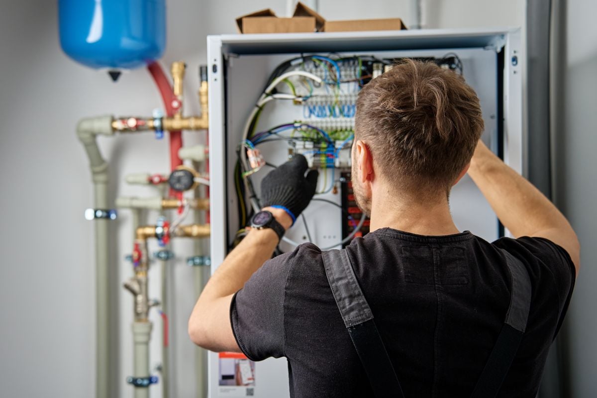 Technician working on internal wiring of heat pump, inspecting electrical connections